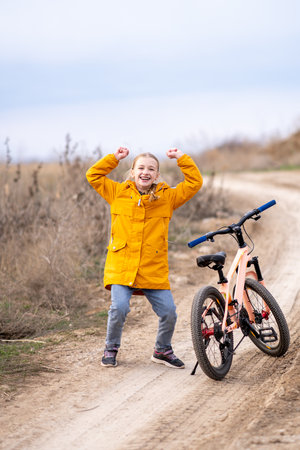 Portrait of a girl expressing emotion of joy, in warm clothes on a bicycle outside the city. Bicycle rides in natureの写真素材