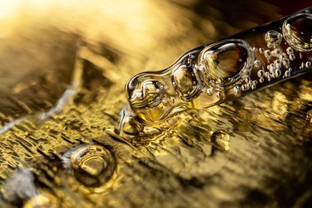 Glass pipette with facial serum on gold background. Essential oil close-up in a pipette. A skin care product with hyaluronic acid in a pipette.の写真素材