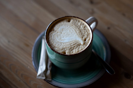 A cup of coffee on a saucer with a portioned packet of sugar. Coffee with a heart
