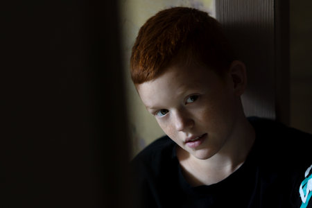 Sad boy with a broken arm in a cast is bored at homeの写真素材