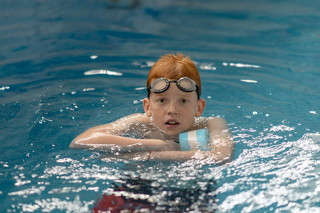 A young boy in a pool learning to swim. A teenager relaxes in the water on a dumbbell for swimming...