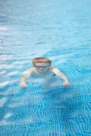 A young athlete in swimming goggles comes out of the water making hand signals while practicing diving in a clear blue pool.の写真素材