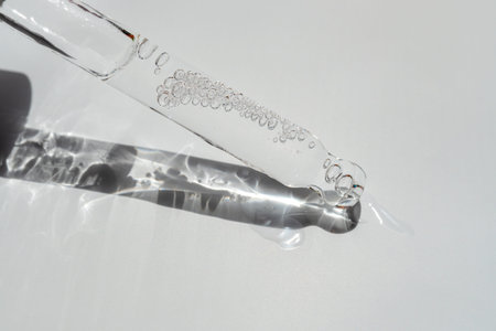 Glass pipette with facial serum on a light background. Essential oil close-up in a pipette. A skin...