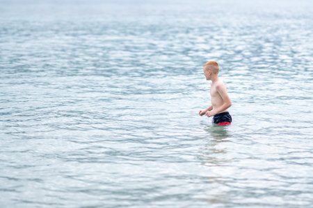 A teenage boy runs into the sea or ocean to swim on a cloudy summer day during a vacation or holidayの写真素材