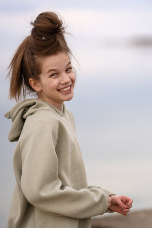 Portrait of a happy girl in a warm hoodie against a blurred horizon between the sky and the seaの写真素材