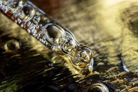 Glass pipette with facial serum on gold background. Essential oil close-up in a pipette. A skin care product with hyaluronic acid in a pipette.の写真素材