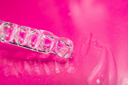 Glass pipette with facial serum on a red background. Essential oil close-up in a pipette. A skin...