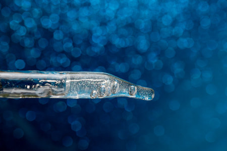 Glass pipette with facial serum on a light background. Essential oil close-up in a pipette. A skin care product in a pipette.の写真素材
