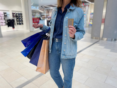 Close up of woman holding in hand credit card standing in shopping center with many bags. Female spent a lot of money at shopping carrying purchases in hand. Shopaholic conceptの写真素材