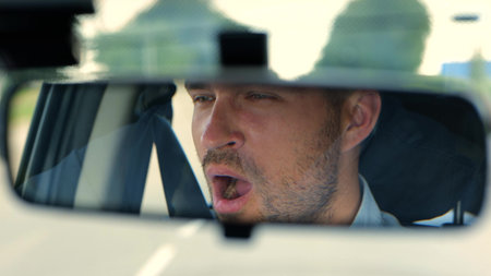 Close up of young tired man inside the car. Handsome Caucasian male driving his car and yawn while...