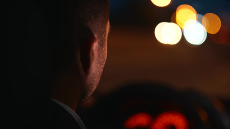 Rear of adult man driver driving a car and looking at the road in the evening. Close up. Back view of businessman drives his automobile at night. Luxury style, blurred backgroundの写真素材