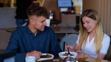 Happy young couple sitting in a cafe. Woman feeding his boyfriend. Couple having lunch in a cafe. Love, dating, food, lifestyle concept. Real timeの写真素材