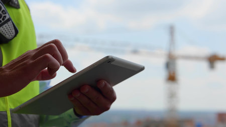Close up of male hands holding tablet gadget tapping and scrolling on screen outdoors. Man builder...