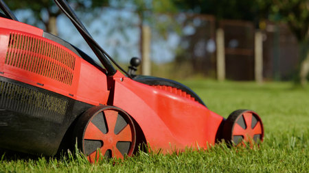 Side view of lawn-mower machine cutting grass outdoors in garden. Close up of an electric lawn mower...