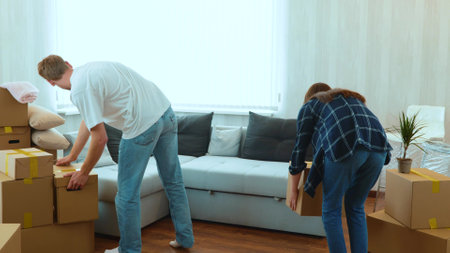 Rear of young couple man and woman entering the room carrying cardboard boxes on moving day and talking. Happy boyfriend and girlfriend moved in together in apartment. Home conceptの写真素材