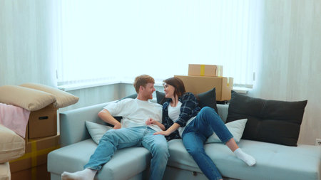 Camera approaching joyful male and pretty female smiling jumping on a sofa in light room with many...