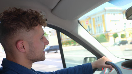 Close up shot of happy Caucasian man driving a car and smiling. Cheerful positive guy with curly...