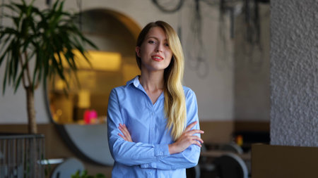 Beautiful young business lady looking at camera and smiling while standing indoors. Portrait of joyful pretty woman in restaurant. Successful entrepreneur. Positive emotionsの写真素材
