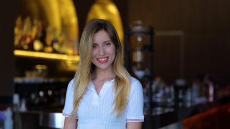 Happy young female smiling and looking at camera indoor in cafe. Beautiful Caucasian carefree blonde woman in restaurant. Positive emotions. Close up portrait. Joyful worker in barの写真素材