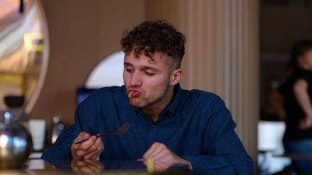Close up of happy young man sitting in cafe indoor and eating wok food. Curly handsome Caucasian guy...