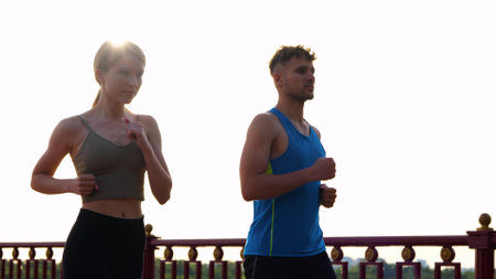 Caucasian happy couple man and woman working out together outside in street. Portrait of young boyfriend and girlfriend jogging outdoors on sunset. Athletic people. Sport activity.の写真素材