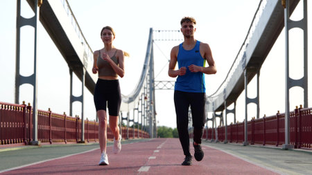 Happy Caucasian young couple of friends running together working out outdoors. Male and female athletes run on the bridge. Sporty athletic activity. Healthy sport, Workout conceptの写真素材