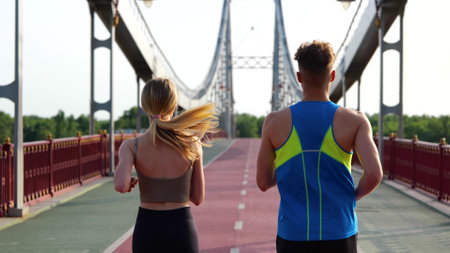 Back view of Caucasian young couple of friends running together working out outdoors. Male and female athletes run on beautiful bridge. Sport activity. Healthy lifestyle conceptの写真素材