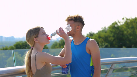Cheerful Caucasian sporty people speaking and drinking water in city after exercising. Male and female athletes smiling and chatting in good mood outdoor. Sport lifestyle conceptの写真素材