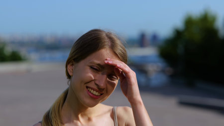 Close up shot of cheerful young female in good mood looking at camera and smiling while standing outside on sunny day and touching her hair. Positive emotions. Slow motionの写真素材
