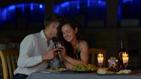 Close up of happy passionate couple in love drinking wine at romantic date and flirting. Handsome loving husband whispering on ear beautiful young wife. Dating conceptの写真素材