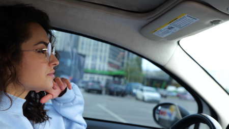 Caucasian young beautiful female in stylish glasses driving a car in city going home after work looking at road turning left. Side view. Close up. Urban lifestyleの写真素材