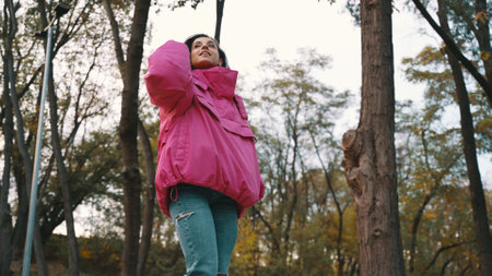 Smiling attractive woman in stylish clothes walking in the park, enjoying the landscape. Low angle. Seasonal style, autumn season concept. Slow motionの写真素材
