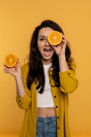 Playful brunette with halves of citrus fruit posing for the camera on the yellow background in the studio. Healthy lifestyle conceptの写真素材