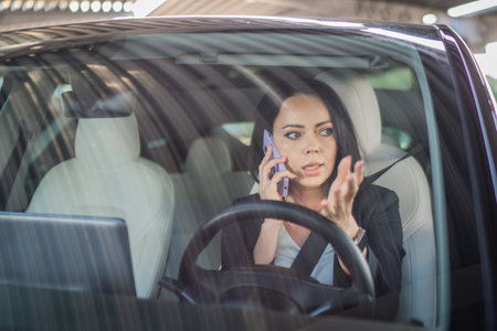 Young businesswoman using safety belt while sitting in the car and talking on mobile phone. Business, road trip, technology, travel conceptの写真素材