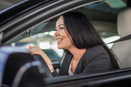 Smiling young Caucasian woman sitting alone on driver seat with fasten belt while driving modern car. Lifestyle and success conceptの写真素材