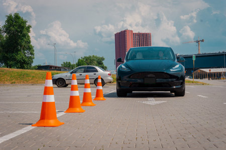 Modern car and safety cones in driving school outdoors. Young female learner driver driving test....