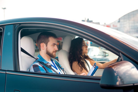 Male instructor holding checklist and writing notes while woman driving during drive lesson. Driving...