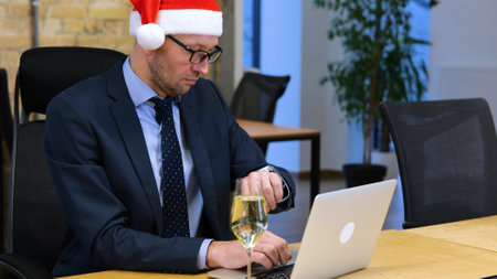 Slow motion video. Caucasian man n black suit and Santa hat is sitting in the office and working, taking off Santa hat and resting a glass of sparkling wineの写真素材