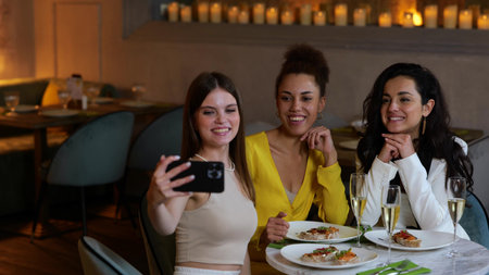 Happy young beautiful women sitting in the restaurant while talking online by video call on the...