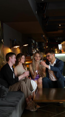 Young friends sitting in restaurant making a toast with whiskey. Lifestyle, party, vertical, social networks concept. Slow motionの写真素材