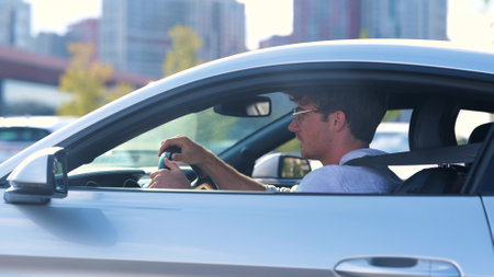 Happy young man in glasses driving his car with open window, looking on the road. Side view. Transport and lifestyle concept. Slow motionの写真素材