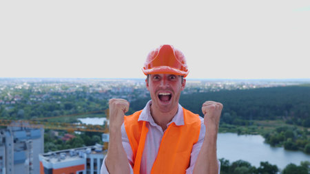 Successful male builder in helmet standing on the roof of construction site while celebrating success. Business, building, industry concept. Slow motionの写真素材