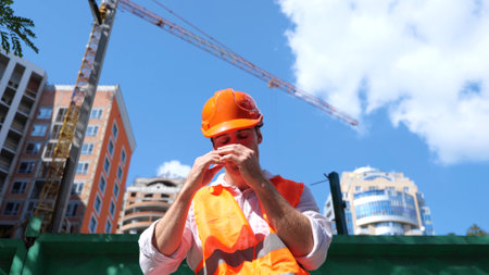 Tired builder in protective helmet sitting on the construction site outdoors. Business, building, industry concept. Slow motionの写真素材