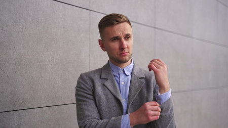 Young man fastening a button the sleeve of shirt, standing outdoors. Slow motion