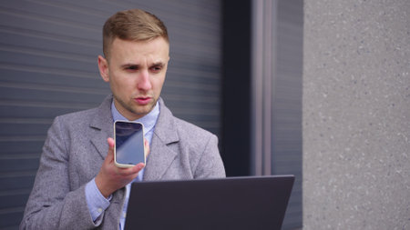 Businessman talking on the mobile phone, holding laptop outdoors. Slow motionの写真素材