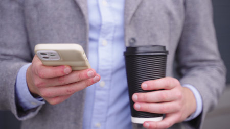 Young man typing on the phone while holding coffee. Slow motionの写真素材