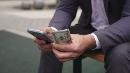 Businessman holding money, using smartphone on the bench. Slow motion