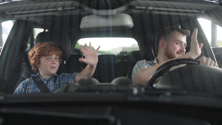 Happy father and his son sitting in the car and waving by hands. Slow motion