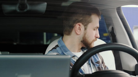 Young man using seat belt, looking at back view mirror in the car.