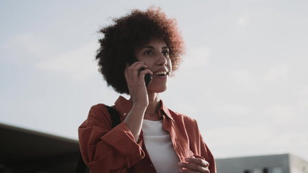 Smiling lady with bag talking on the smartphone outside.